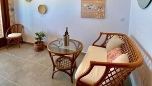 Een gezellige zithoek met rieten meubels, een ronde glazen tafel en decoratieve wandkunst.