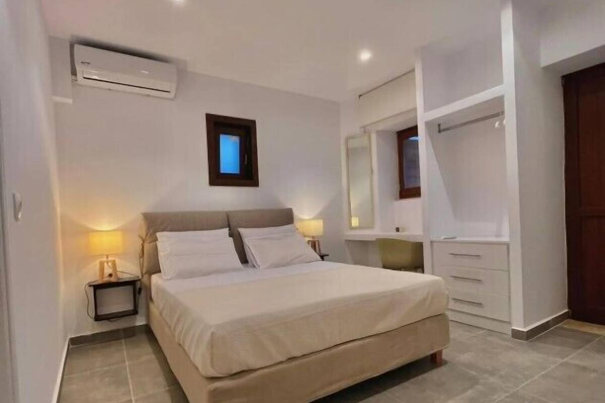 A bedroom with a bed, bedside tables, a mirror, and an air conditioning unit.