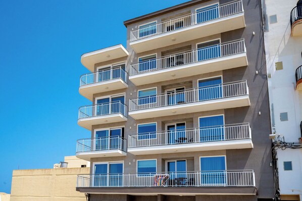 A multi-story residential building with balconies, large windows, and a clear blue sky.