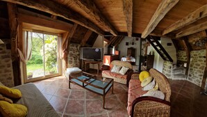 A rustic interior with a wooden ceiling, a TV, wicker furniture, and a stone wall. - Le Puy D'aubrac, Maison Familiale en Pleine Campagne (Florentin-la-Capelle)