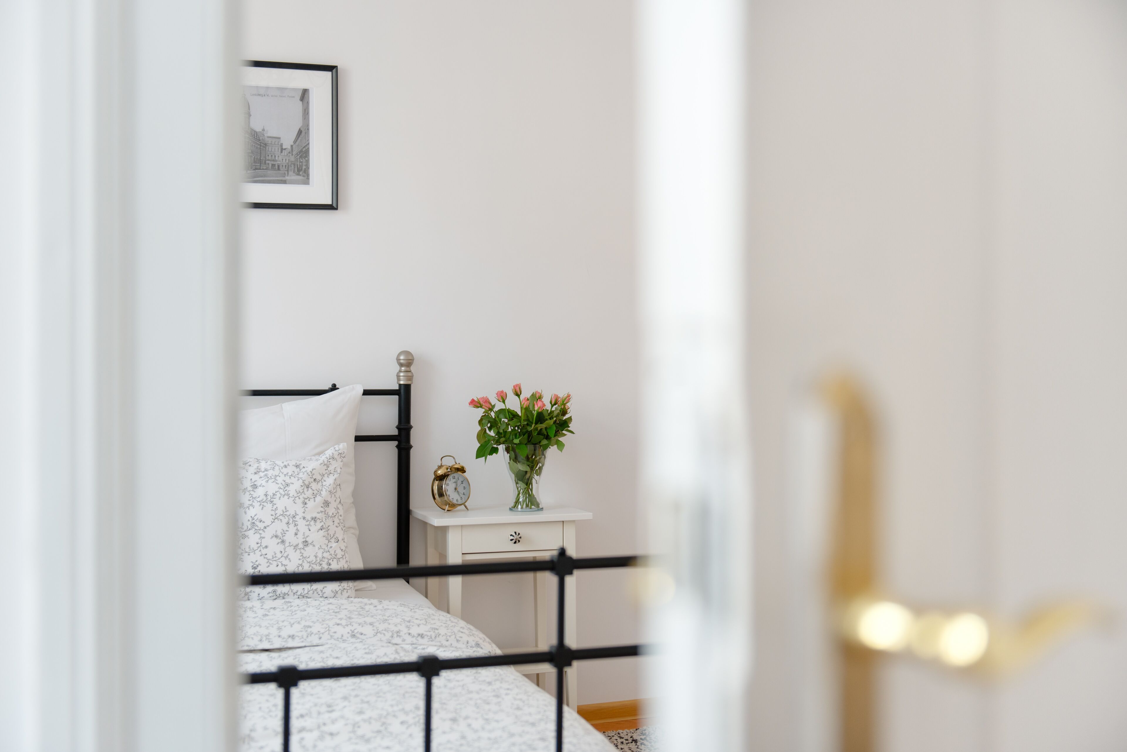 Een slaapkamer met een bed, een nachtkastje, een lijst met een afbeelding aan de muur en een deur.