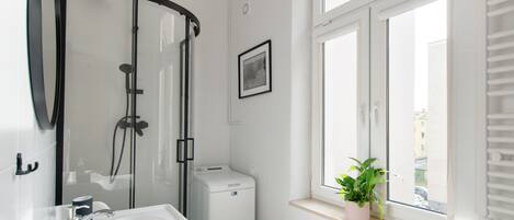 Ein modernes Badezimmer mit einer Duschkabine aus Glas, einer integrierten Waschmaschine und einem Fenster mit Pflanze.