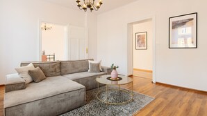 Un salon moderne avec un canapé d’angle, une table basse ronde, un lustre et des œuvres d’art encadrées accrochées aux murs.