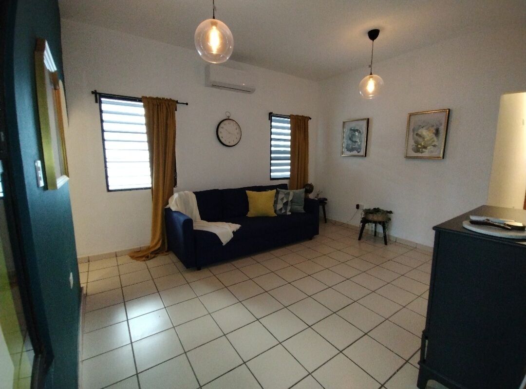 A living room with a sofa, two windows with curtains, a clock, and a small table.