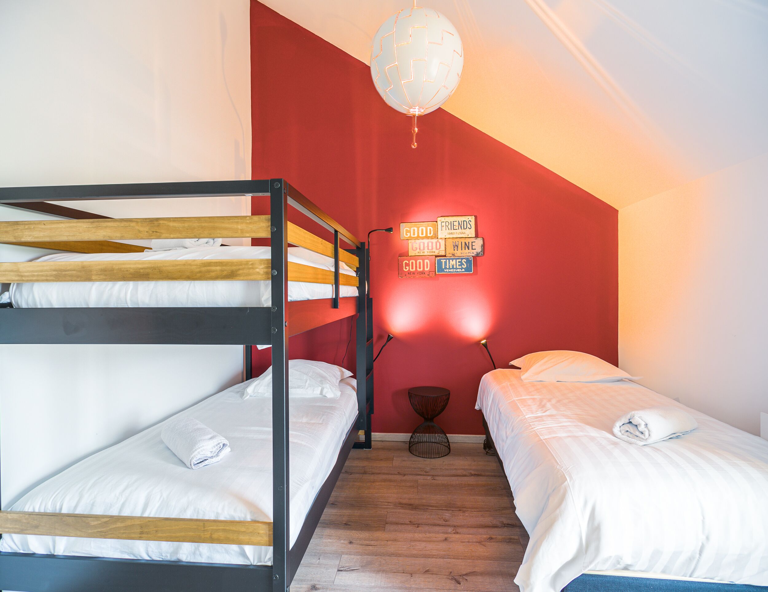 Ein Schlafsaalzimmer mit Etagenbetten, einer roten Wand, einer Globenlampe und einer Wand mit motivierenden Sprüchen.