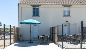 Un edificio con tetto in tegole, un patio recintato con tavolo e sedie e un ombrello blu.