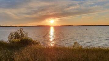 A sunset over a calm lake with distant land visible on the horizon.