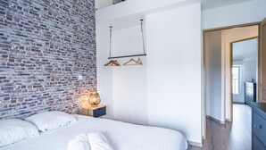Una camera da letto con parete in mattoni, un letto con biancheria bianca, un comodino con una lampada e un armadio.