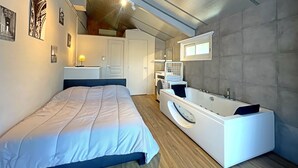 A modern bedroom with a large bed, a built-in washing machine, a bathtub, and a lofted sleeping area. - Magnifique Villa Avec vue sur le Luberon (Robion)
