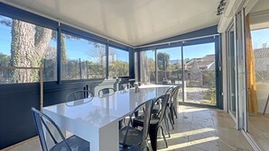 A modern dining area with a large table and chairs, large windows offering a view of the outdoors, and a ceiling with recessed lighting. - Magnifique Villa Avec vue sur le Luberon (Robion)