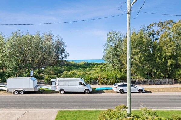 A white van and a trailer on a road with a view of a body of water and trees.
