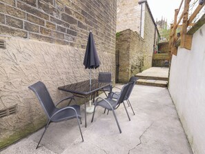 An outdoor patio with a table and four chairs, a black umbrella, and a stone wall. - Erin Cottage (Keighley)