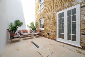 A patio with a table and chairs, a brick wall, and a sliding glass door.