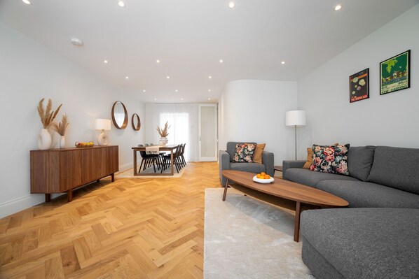 A modern living room with a grey sofa, wooden coffee table, and a dining area with a wooden cabinet and table.