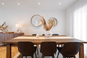 A modern dining area with a wooden table, dark chairs, a vase with pampas grass, two round mirrors, and a lamp on a wooden cabinet.