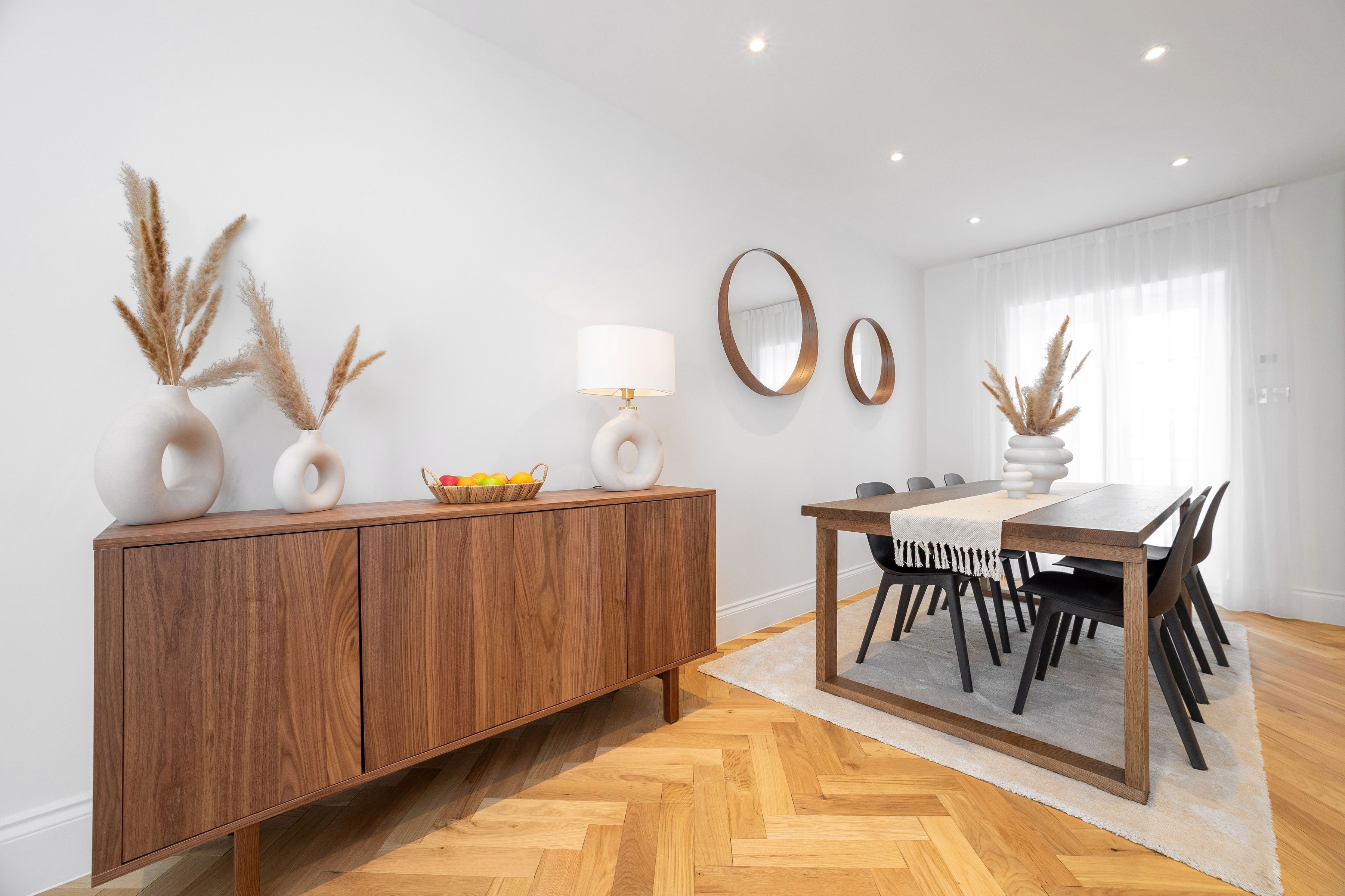 Un comedor con un armario de madera, una mesa con sillas y jarrones decorativos con plumas de pluma.