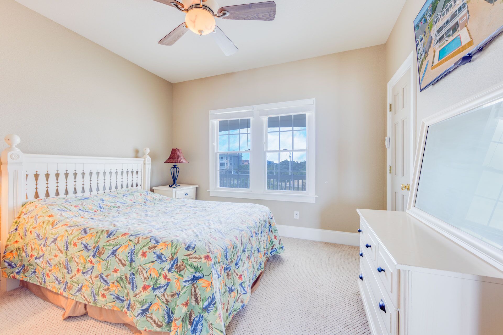A bedroom with a bed, a nightstand, a lamp, a dresser, a window, and a ceiling fan.