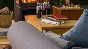 Ein gemütliches Wohnzimmer mit Kamin, einer Couch, einem Schachbrett und einem Tisch mit Büchern und Weingläsern.
