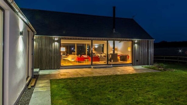 Ein modernes Haus mit einem großen Glasfenster, das in einen Wohnbereich mit roten Möbeln führt.