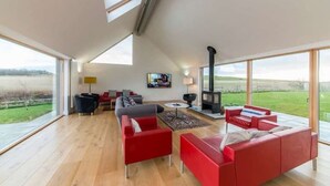 Ein geräumiges Wohnzimmer mit hohen Decken, großen Fenstern, einem Kamin und einem Fernseher.