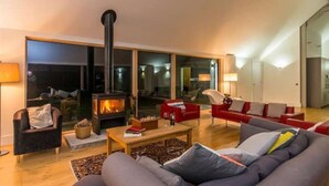 Ein großzügiges Wohnzimmer mit einem großen Kamin, bequemen Sitzmöglichkeiten und Blick durch große Glasschwingtüren.