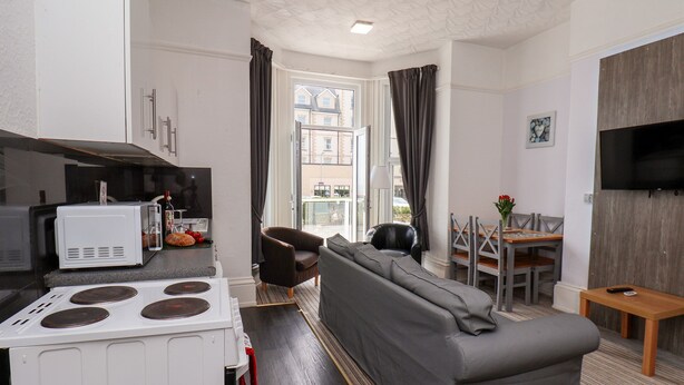 A compact living space with a kitchenette, a grey sofa, a dining area with a table and chairs, and a TV mounted on the wall. - Beach (Bridlington)