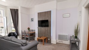 A modern living room with a grey sofa, a dining table with chairs, a TV mounted on a wooden door, and a small plant on a side table. - Beach (Bridlington)