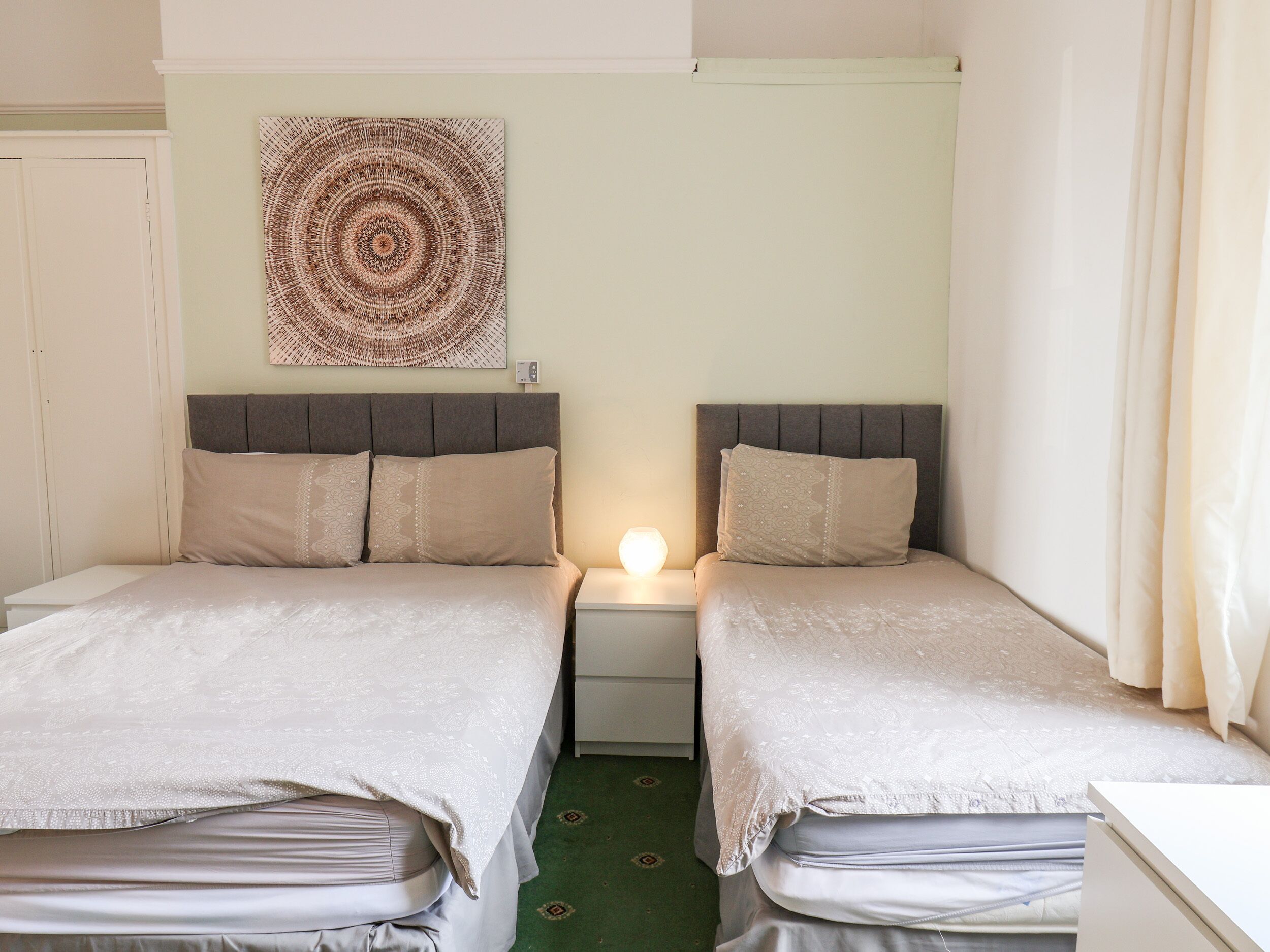 Ein Doppelzimmer mit zwei Betten, einem Wandbild und einer Nachttischlampe.