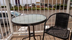 A balcony with a round table and a wicker chair, overlooking a street with parked cars and buildings. - Beach (Bridlington)