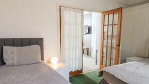 A hotel room with two beds, a nightstand with a lamp, a green carpet, and a wooden door leading to a balcony. - Beach (Bridlington)