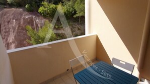 En balkon med et bord og stole, udsigt til træer og et klippefyldt område, samt et vandmærke med teksten "Vacances Sote".