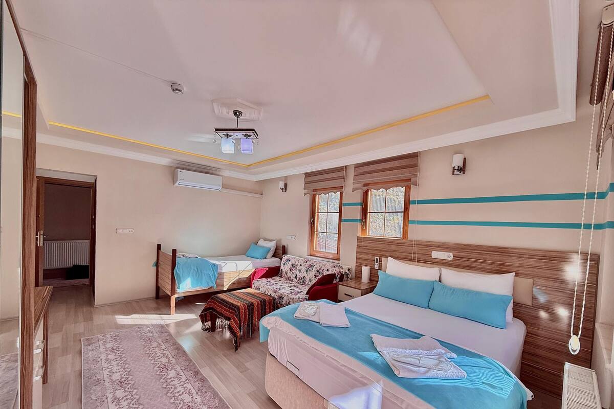 Habitació d'hotel amb un llit gran, un llit més petit, un sofà, un escriptori i una finestra amb cortines.