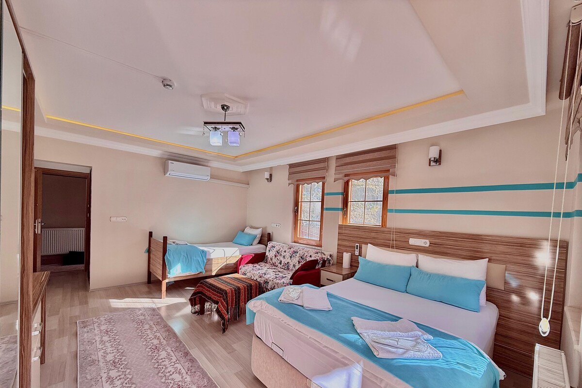 A hotel room with a large bed, a smaller bed, a sofa, a desk, and a window with curtains.