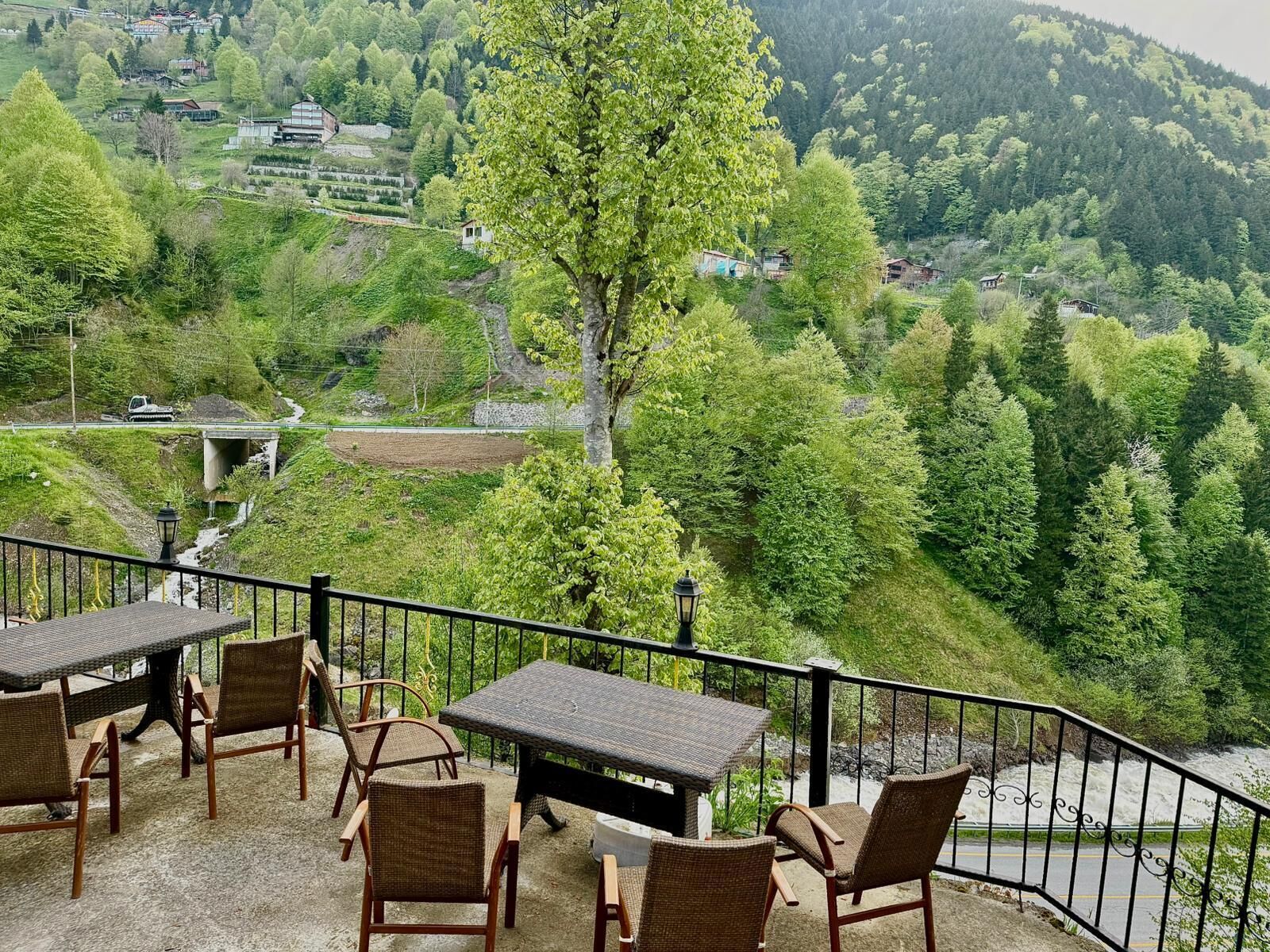 A terrace with wicker furniture, a table, and chairs overlooking a mountainous landscape with greenery and buildings.