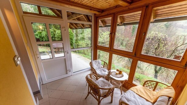 A cozy room with a large window, wicker furniture, and a view of the outdoors. - Villa Dolina Miru (Zavrc)