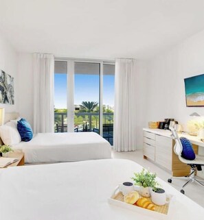 Habitación de hotel con dos camas, un escritorio, una silla, un ventanal con cortinas y un cuadro en la pared.