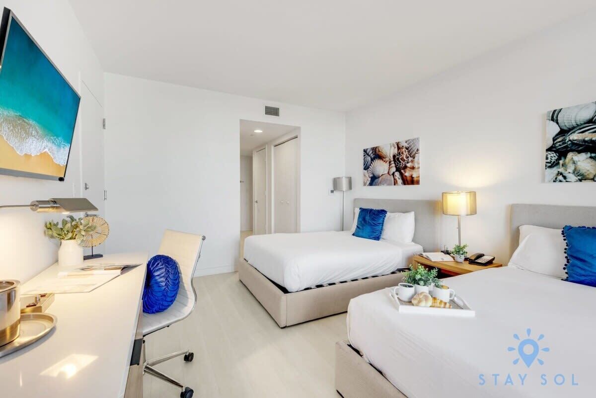 Una habitación de hotel con cama, mesita de noche, lámpara y obras de arte en las paredes.