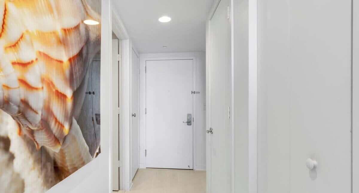 Ein Flur mit einer weißen Tür am Ende, einem Lichtschalter an der Wand und einer Deckenleuchte.