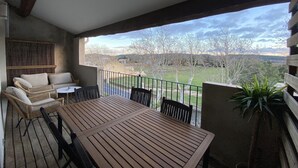 A balcony with a wooden table and chairs, a view of a rural landscape, and a potted plant. - T4 Bord Canal du Midi, Piscine (Homps)