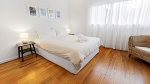 Un dormitori amb un llit, una tauleta de nit, una cadira i una finestra amb cortines.