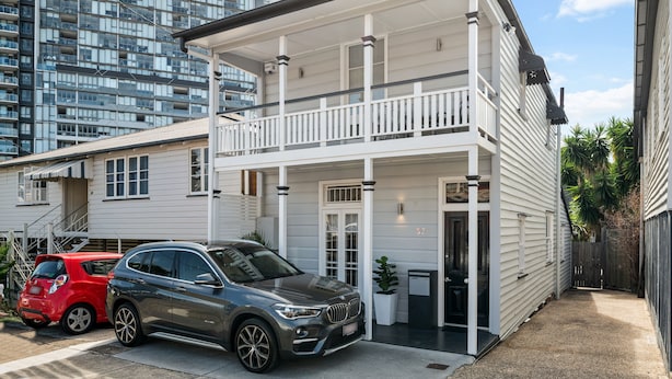 Une maison à deux étages avec un balcon, un garage et une allée où sont garées deux voitures.