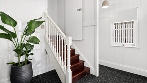 Un escalier avec des rampes blanches et des marches en bois, une plante en pot et un luminaire suspendu.