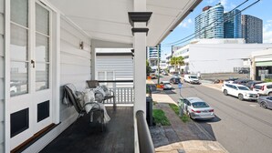 Un balcon donnant sur une rue de la ville, avec une voiture garée et un immeuble à la façade bleue.
