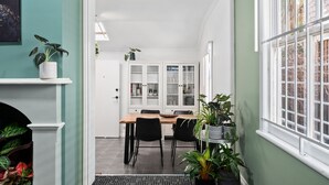 Un coin repas avec une table et des chaises en bois, un buffet blanc aux portes vitrées et des plantes en pot.
