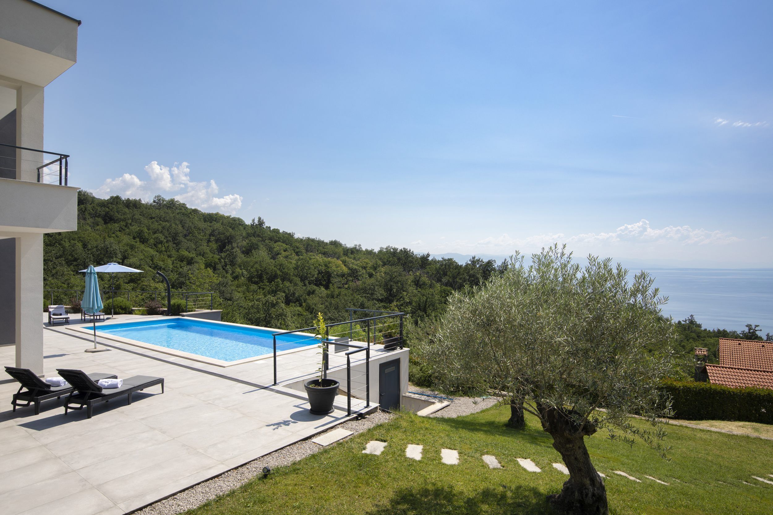 A modern outdoor pool area with lounge chairs, a potted plant, and a view of the sea.