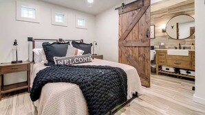 Une chambre à coucher comprenant un lit, une table de chevet, une commode, un miroir et une porte coulissante de style rustique.