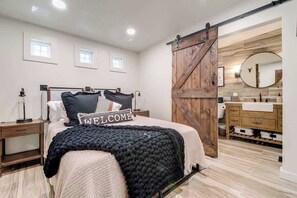 Un dormitorio con cama, mesita de noche, cómoda, espejo y una puerta corrediza tipo granero.