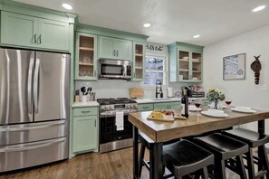 A kitchen with a stainless steel refrigerator, a microwave, a stove, and a dining table with chairs.