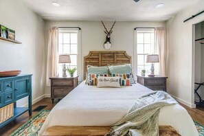 A bedroom with a wooden headboard, two bedside tables with lamps, a decorative antler on the wall, and a bed with colorful pillows.