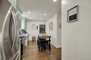 Une cuisine moderne dotée d’appareils électroménagers en acier inoxydable, un coin repas avec une table en bois et des tabourets de bar noirs, et un panneau décoratif encadré accroché au mur.